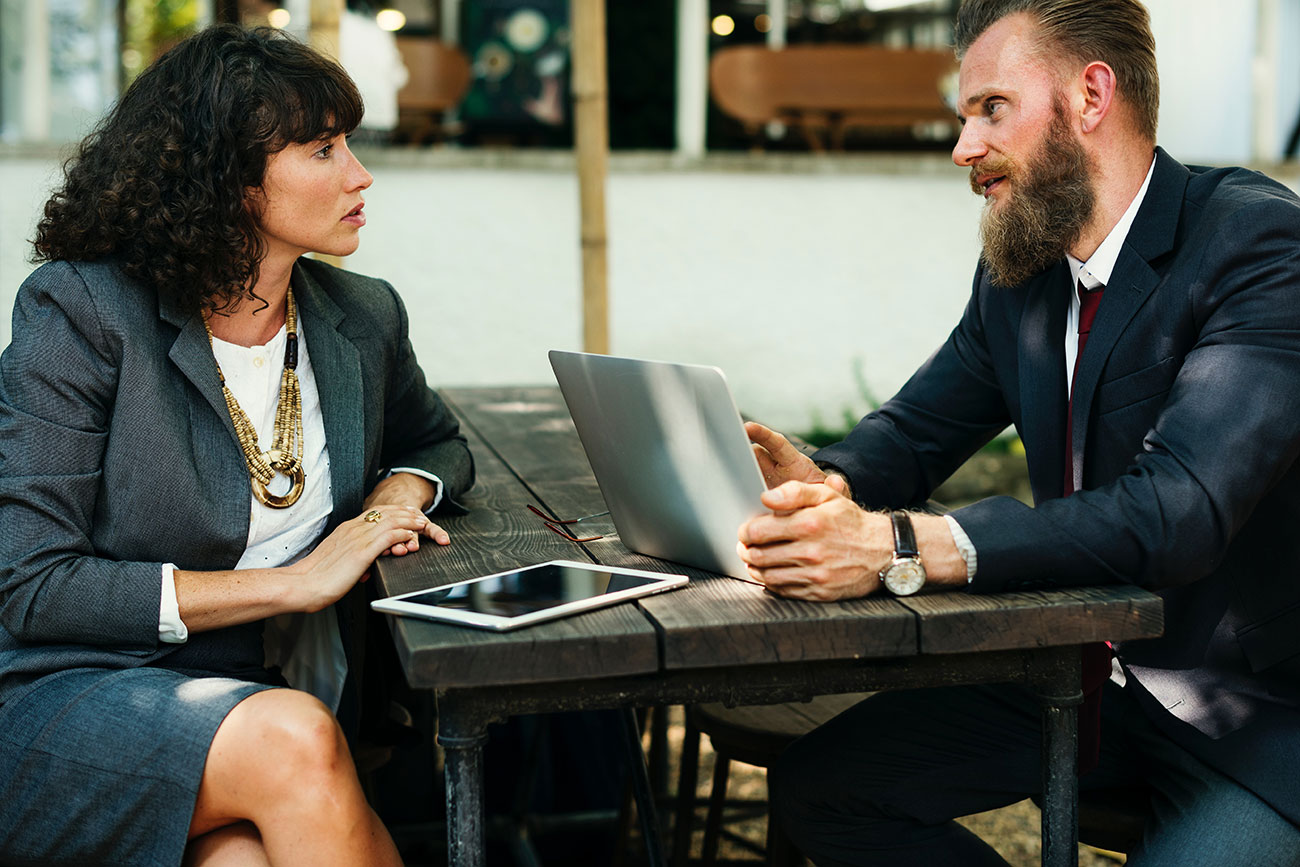 Dos profesionales conversando en una reunión de negocios con un portátil y una tableta